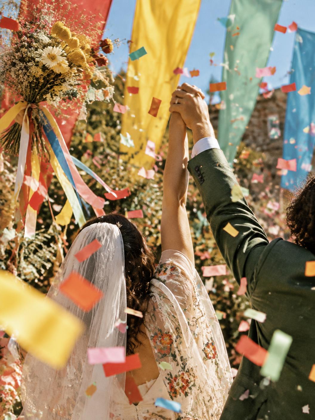 A joyful ceremony celebration — raised hands, rainbow confetti and colourful fabric banners